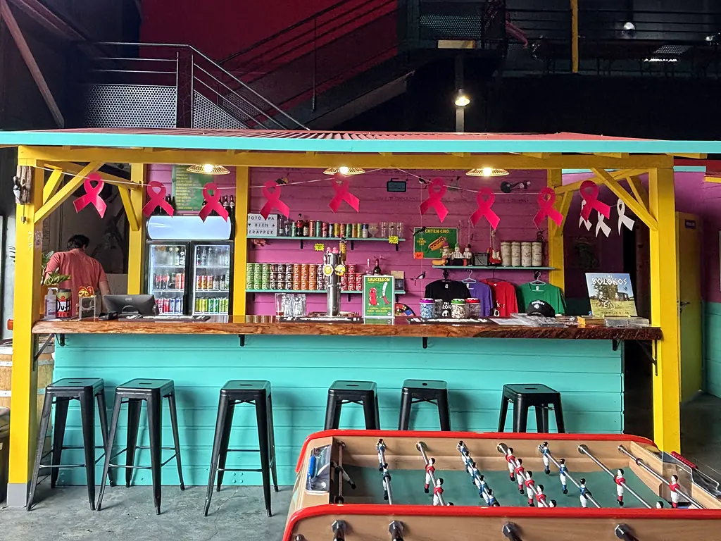 Le bar en forme de case, turquoise et jaune sous son toit de tôle rouge, avec le babyfoot devant.