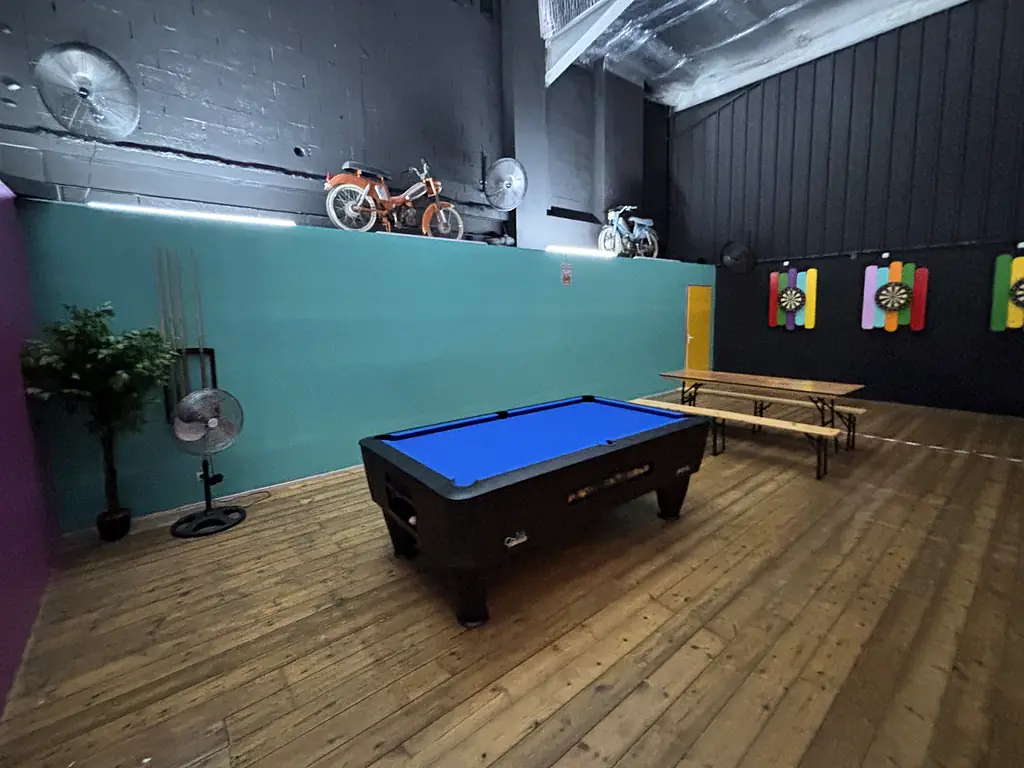 Le billard au tapis bleu sur la mezzanine, avec des cibles de fléchettes et deux mobylettes anciennes au mur.